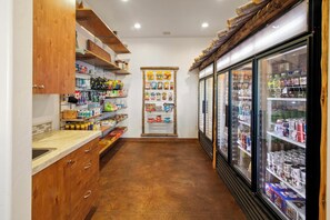 A narrow hallway with wooden cabinets on the left, a central display of snacks, and refrigerated beverage cases on the right.