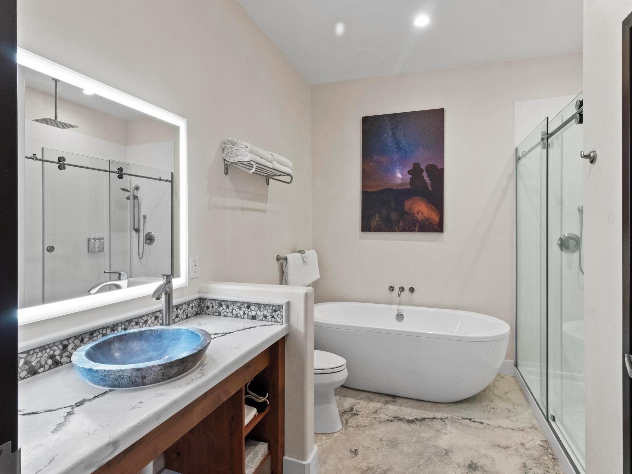 A modern bathroom with a large mirror, a freestanding bathtub, and a glass-enclosed shower.