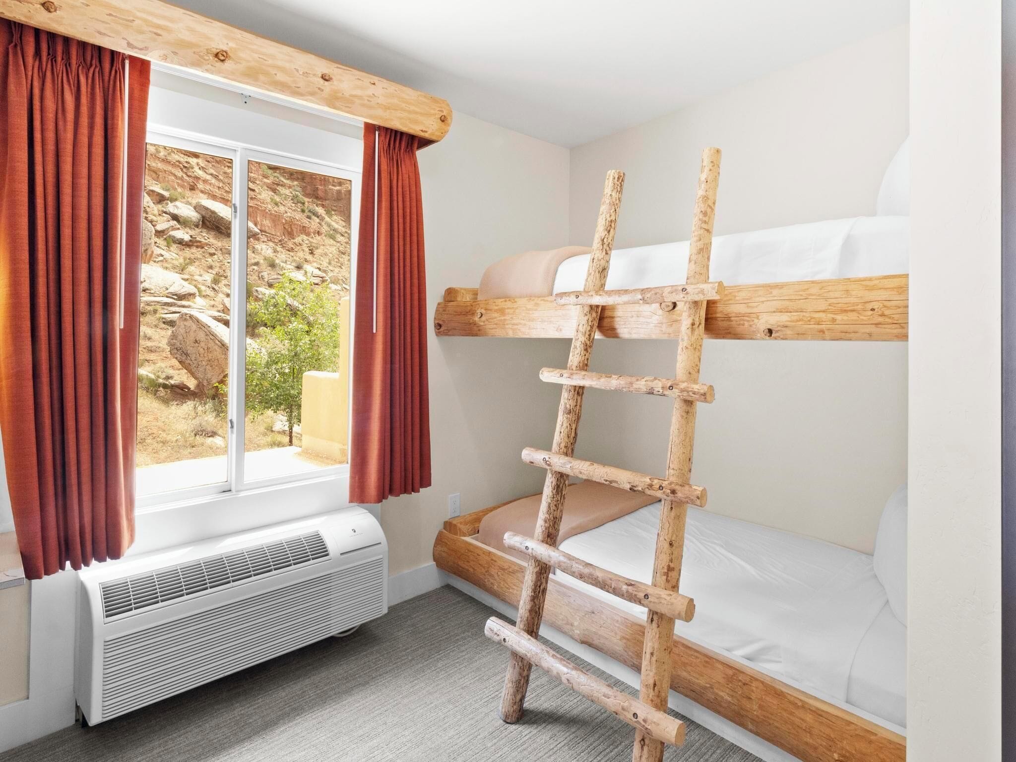 A bunk bed with a wooden ladder, a window with curtains, and a white air conditioner.