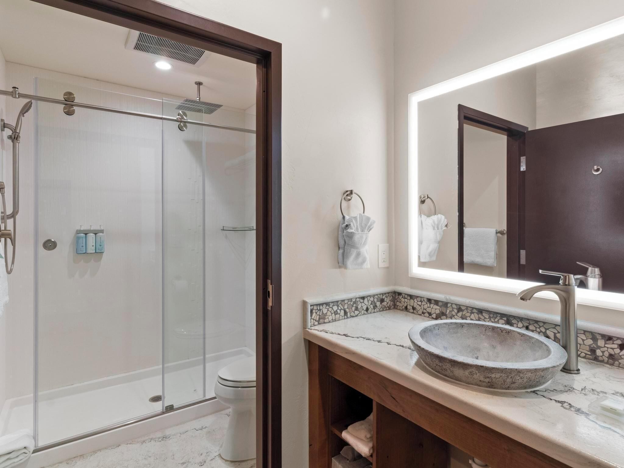 A modern bathroom with a glass-enclosed shower, a marble sink, and a large mirror.