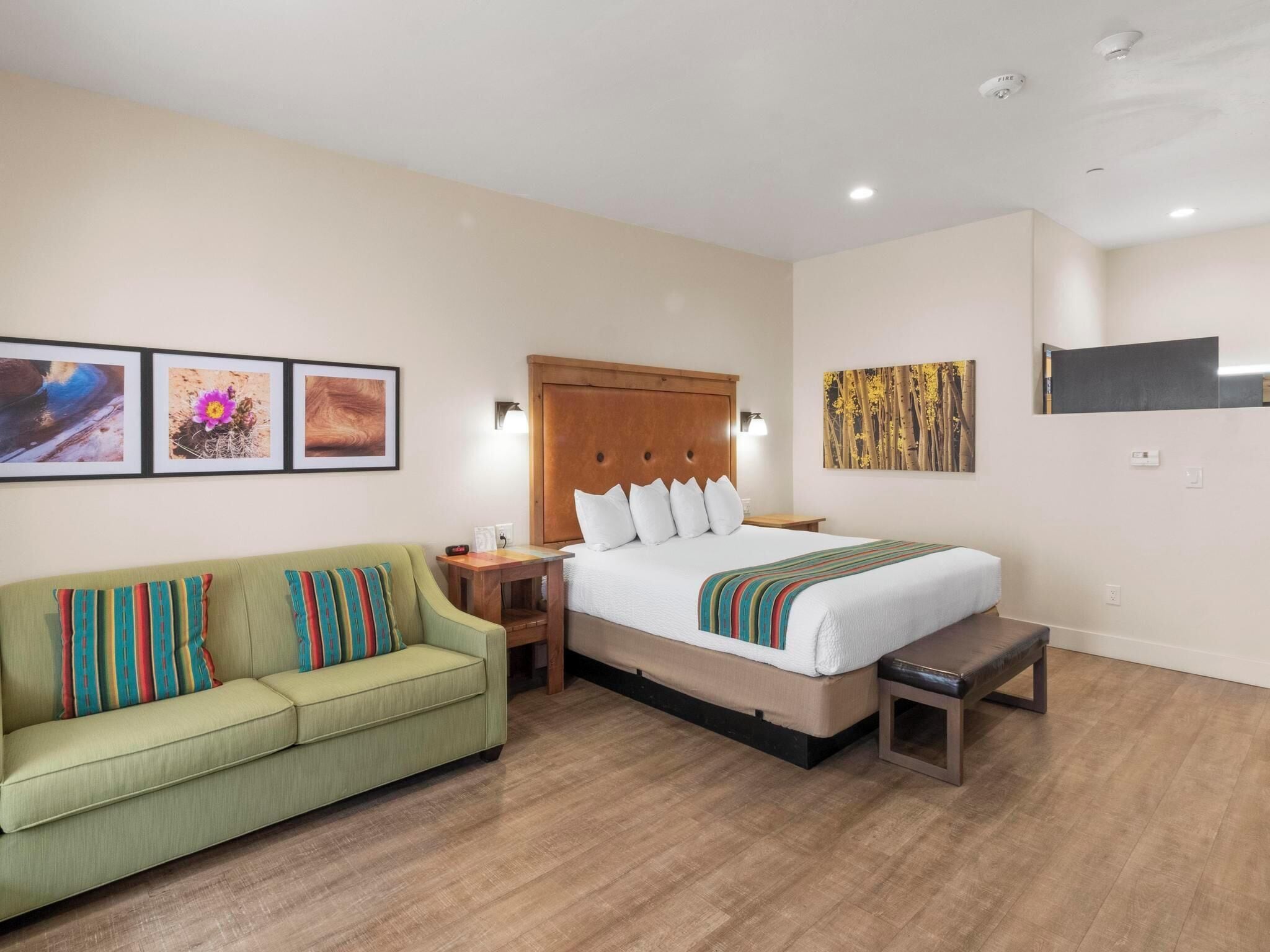 A hotel room with a bed, a green sofa, a wooden bench, and artwork on the walls.