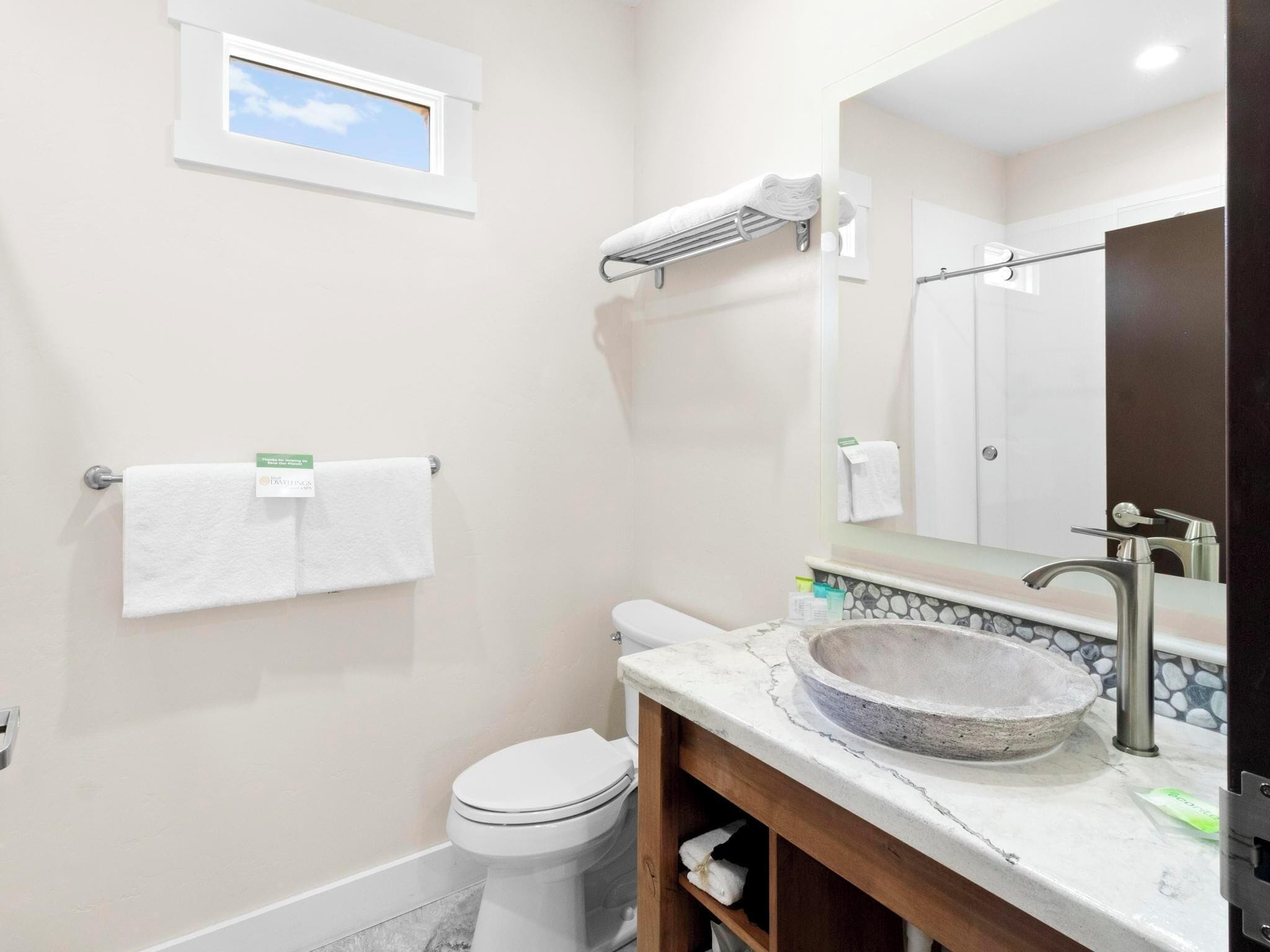 A bathroom with a toilet, a sink with a stone basin, a towel rack, and a window with a view of the sky.