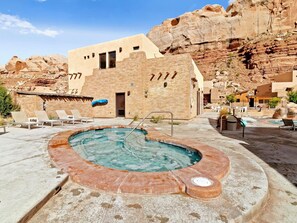Un área de piscina con sillones reclinables, un jacuzzi y vistas a acantilados rocosos.