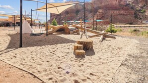 A sandy playground with wooden structures and a teepee.