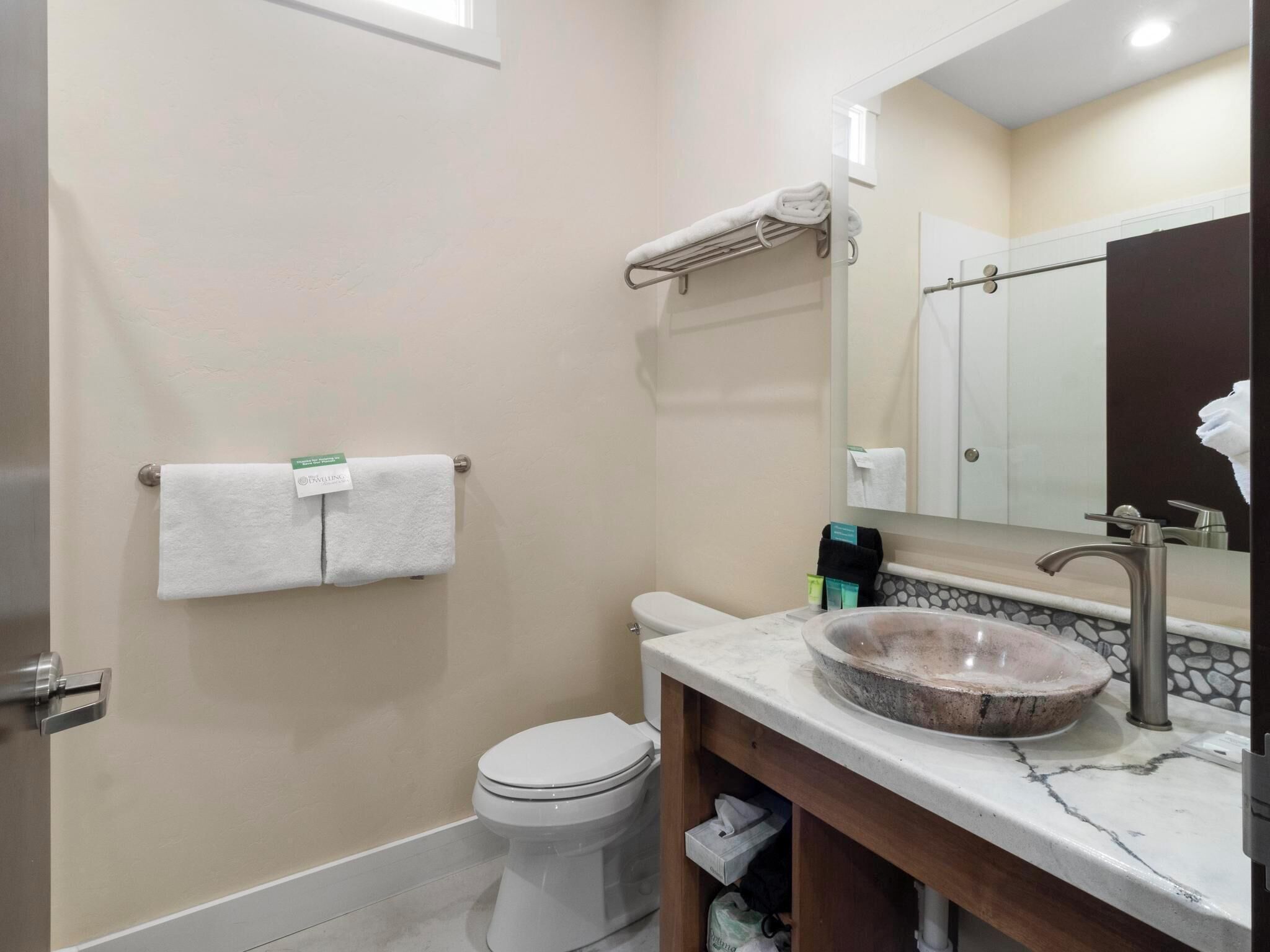 A bathroom with a toilet, a sink with a stone basin, a towel rack with two towels, and a mirror above the sink.