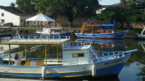 A marina with several boats docked, a white building with a tiled roof, and a stone wall with vegetation. - Pousada Bela Paraty (Paraty)