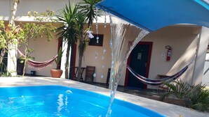 A swimming pool with clear blue water, a hammock, and a door with a fire extinguisher. - Pousada Bela Paraty (Paraty)