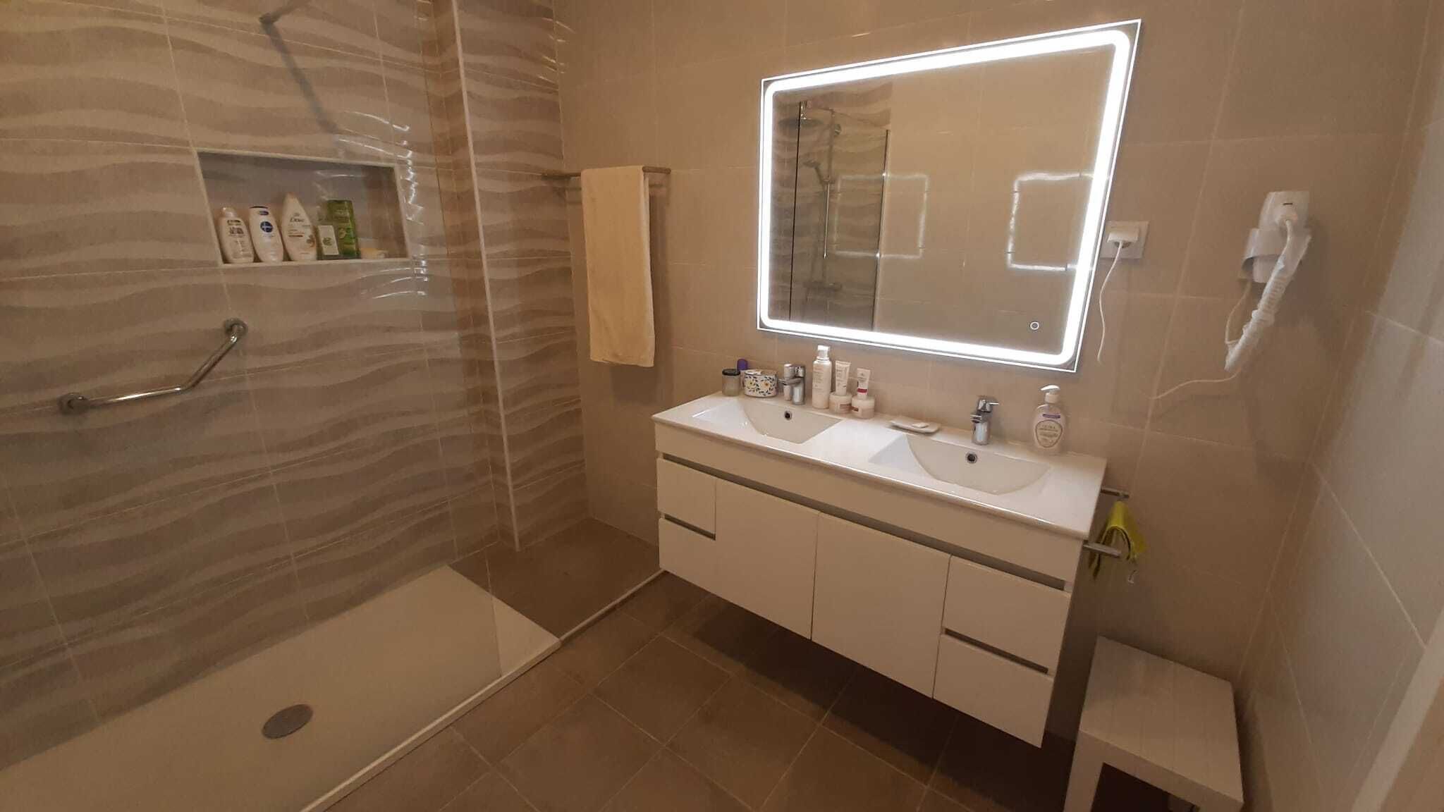 Uma casa de banho moderna com chuveiro envidraçado, duas pias, um espelho grande e toucador com armários.