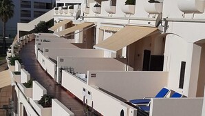 Ein modernes Hotel mit Dachterrasse, weißen Wänden und Balkonen mit Blumentöpfen.
