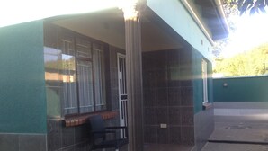 A building with a green exterior, a window with a patterned curtain, a chair, and a tiled floor. - Eliba Apartments (Livingstone)