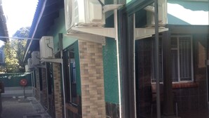 A building exterior with multiple air conditioning units mounted on the wall, a tiled walkway, and a window with a view of the interior. - Eliba Apartments (Livingstone)