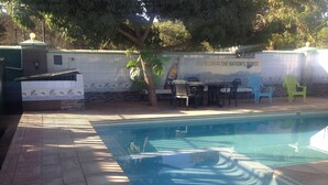 A swimming pool with a tiled deck, a mural on the wall, and outdoor seating. - Eliba Apartments (Livingstone)