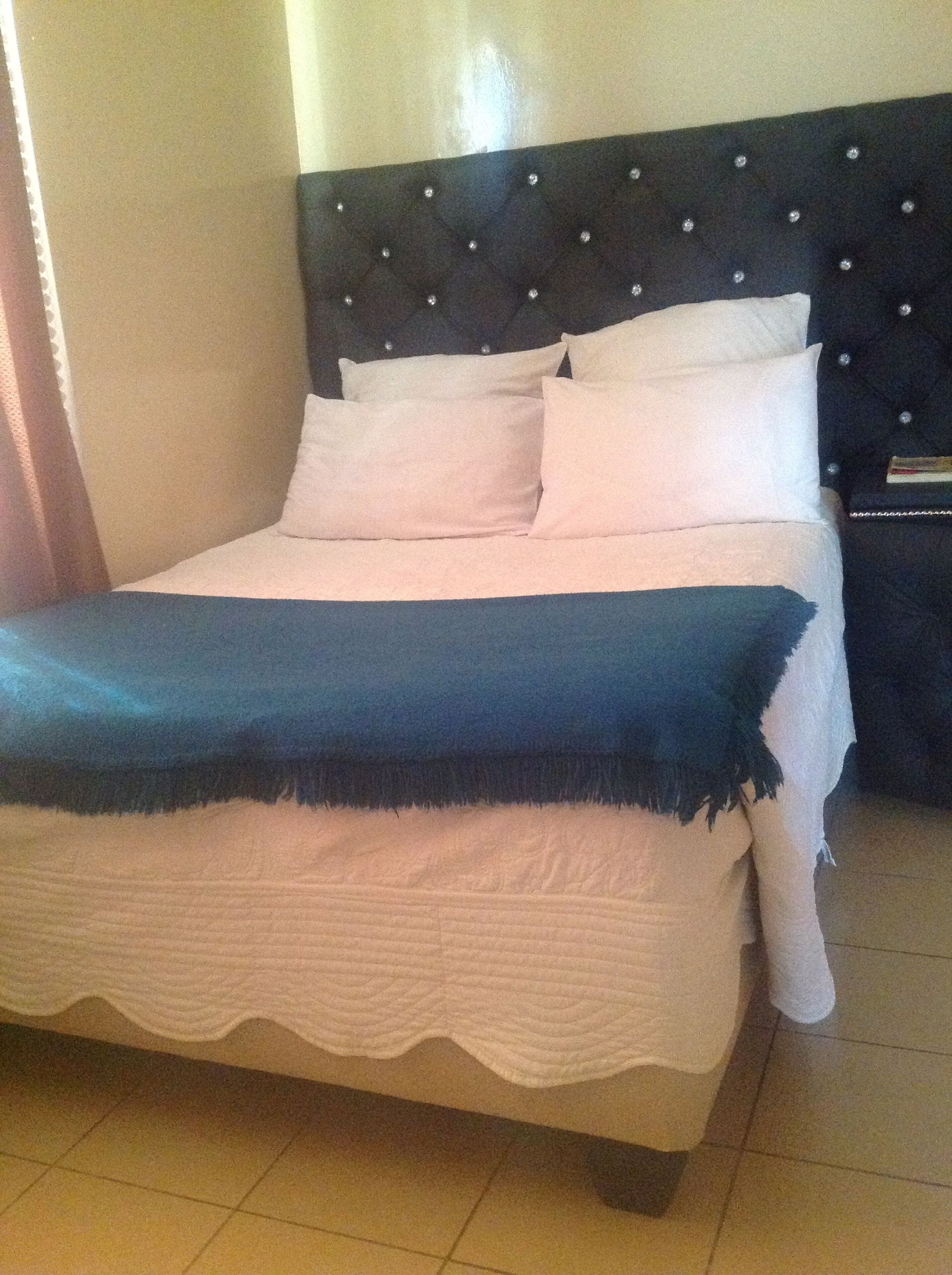 A bed with a tufted headboard, white bedding, and a blue throw blanket.