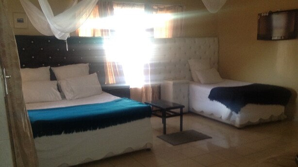 A room with a bed, a sofa, a small table, and a TV on the wall. - Eliba Apartments (Livingstone)