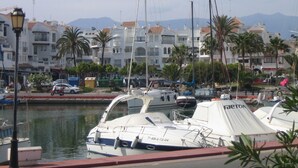 Un port de plaisance où sont amarrés des bateaux, entouré de bâtiments dotés de balcons et de palmiers.