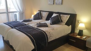 Un lit double avec une couvre-lit noir et blanc, plusieurs oreillers et une table de chevet avec une lampe.