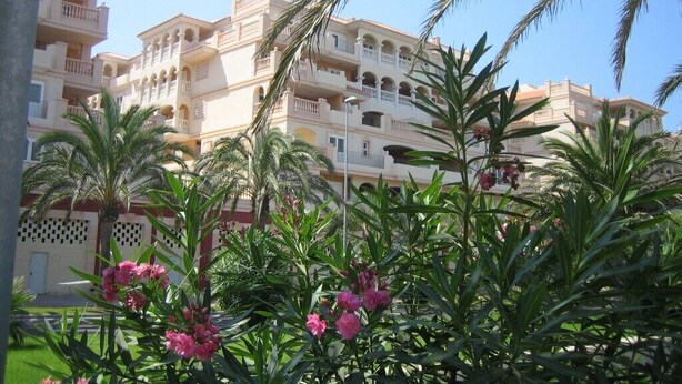 Un immeuble à plusieurs étages doté de balcons et d’un jardin où poussent des fleurs roses.