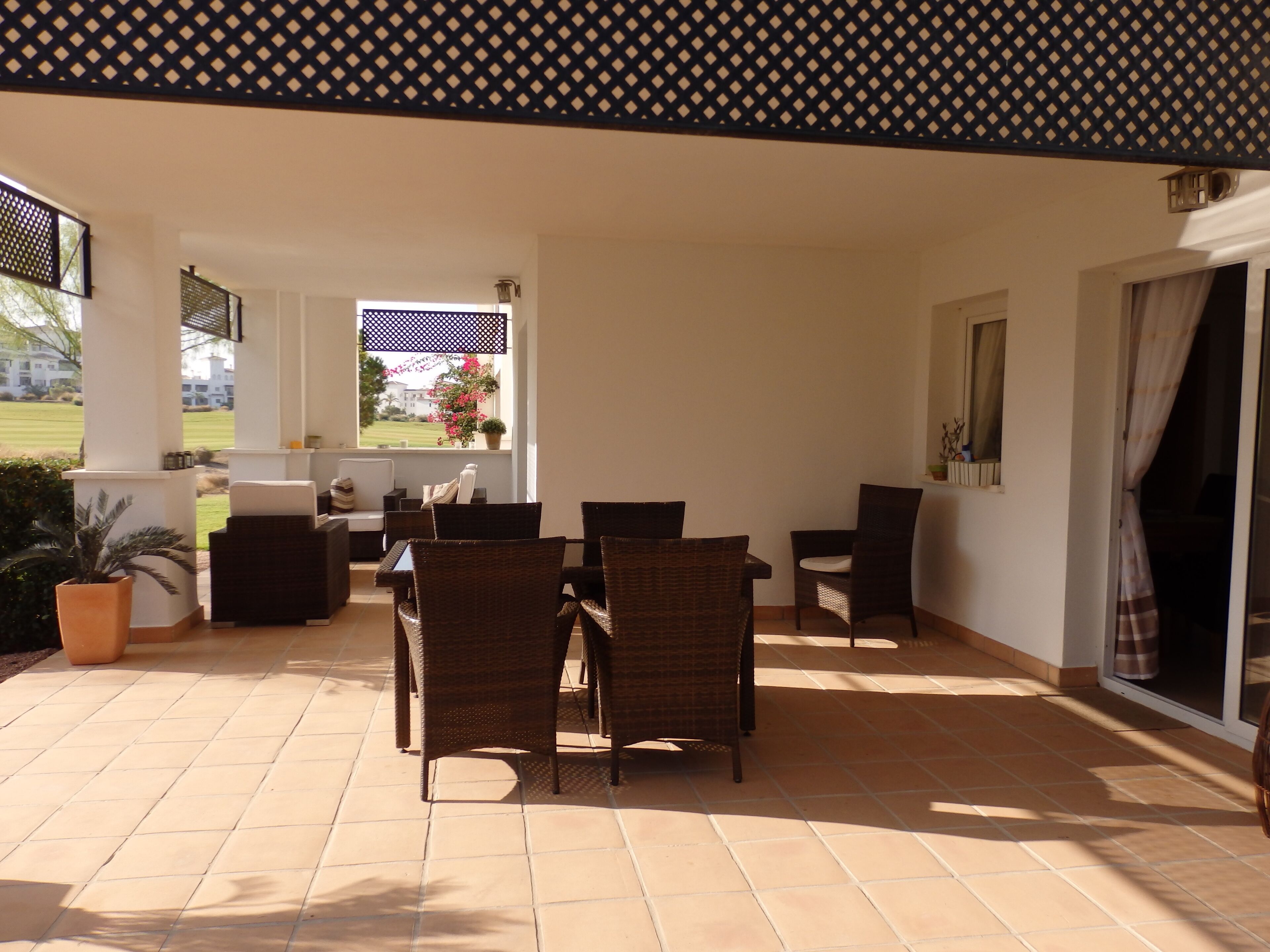 A covered patio area with wicker furniture, a view of a garden, and a window overlooking the landscape.