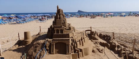 A large sandcastle on a beach with a clear sky.