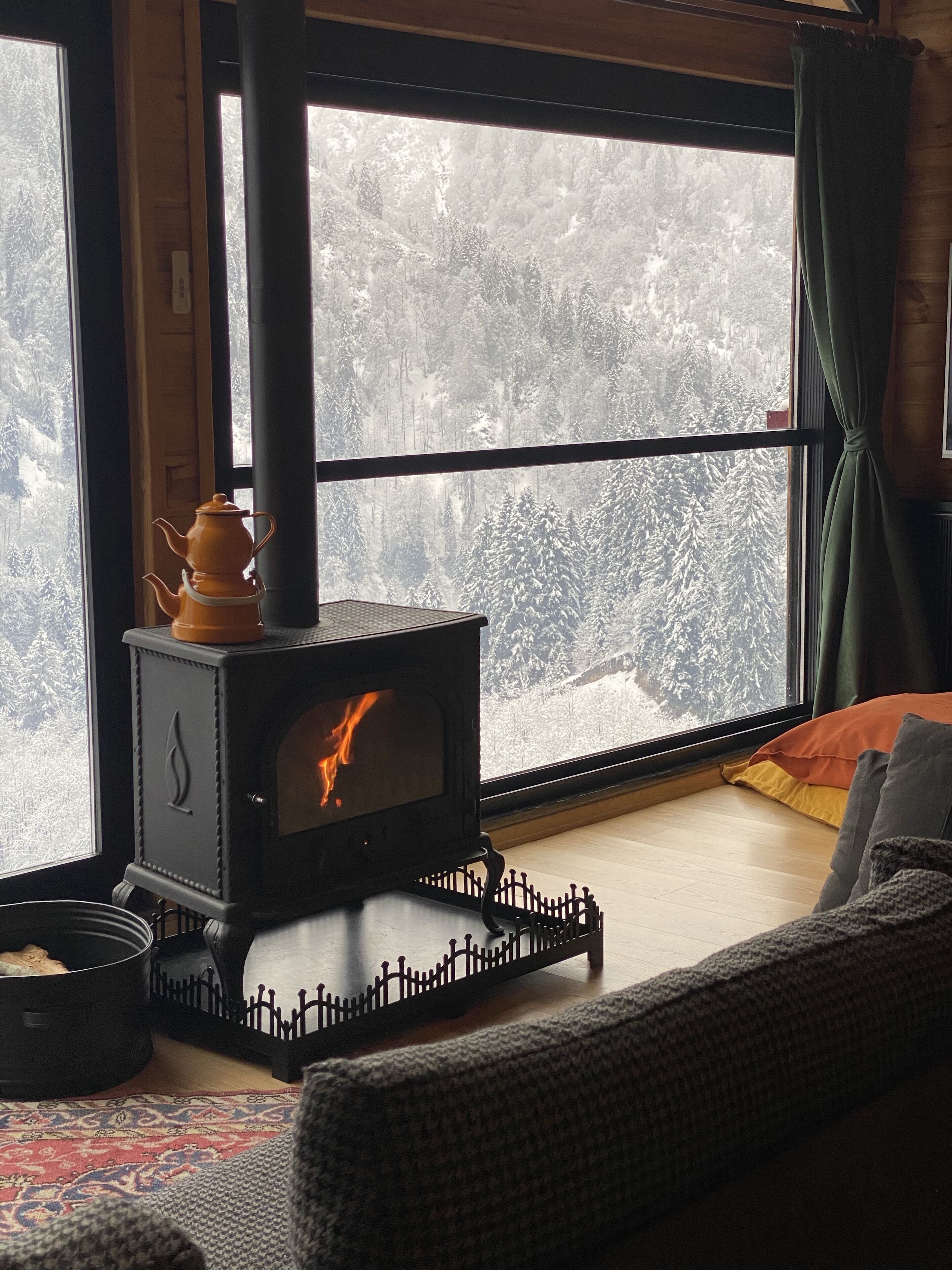 Ett mysigt rum med en vedeldad kamin, ett fönster med utsikt över ett snötäckt landskap och en mönstrad matta.