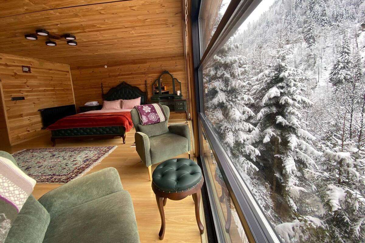 Ein gemütliches Blockhaus-Zimmer mit einem großen Fenster mit Blick auf einen verschneiten Wald.
