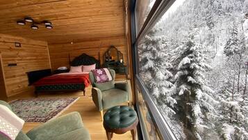 Acogedora habitación en una cabaña de troncos con un ventanal grande que da a un bosque nevado.