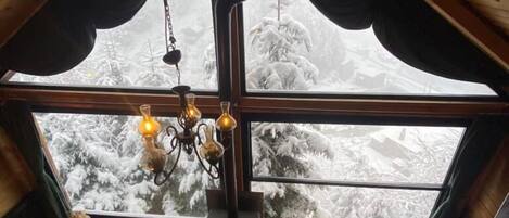 A cozy room with a high ceiling, a fireplace, and a large window offering a snowy view.