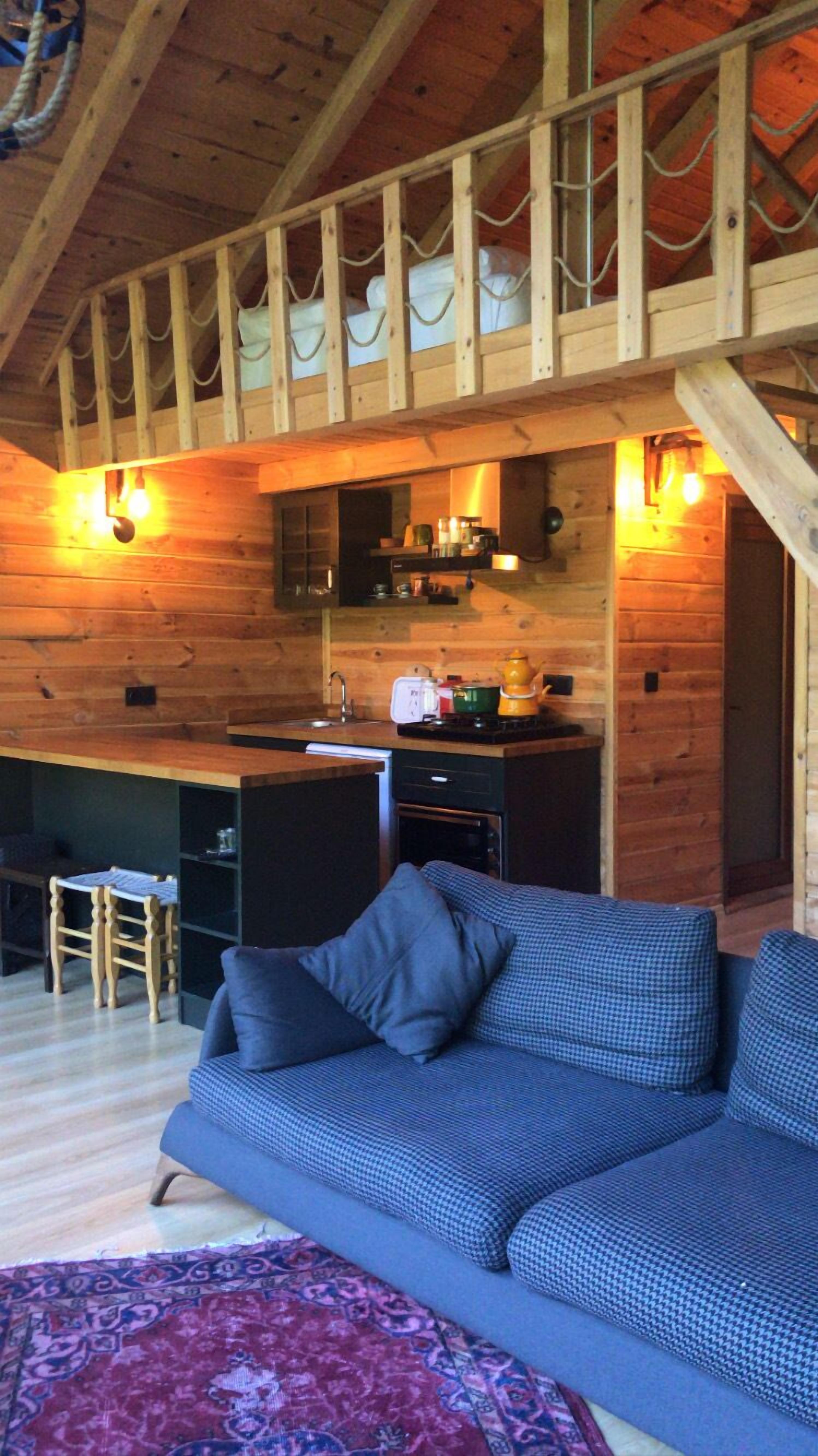 Un interior de cabaña acogedor con techo de madera, kitchenette, sofá y alfombra estampada.