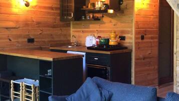 A cozy cabin interior with a wooden ceiling, a kitchenette, a sofa, and a patterned rug.