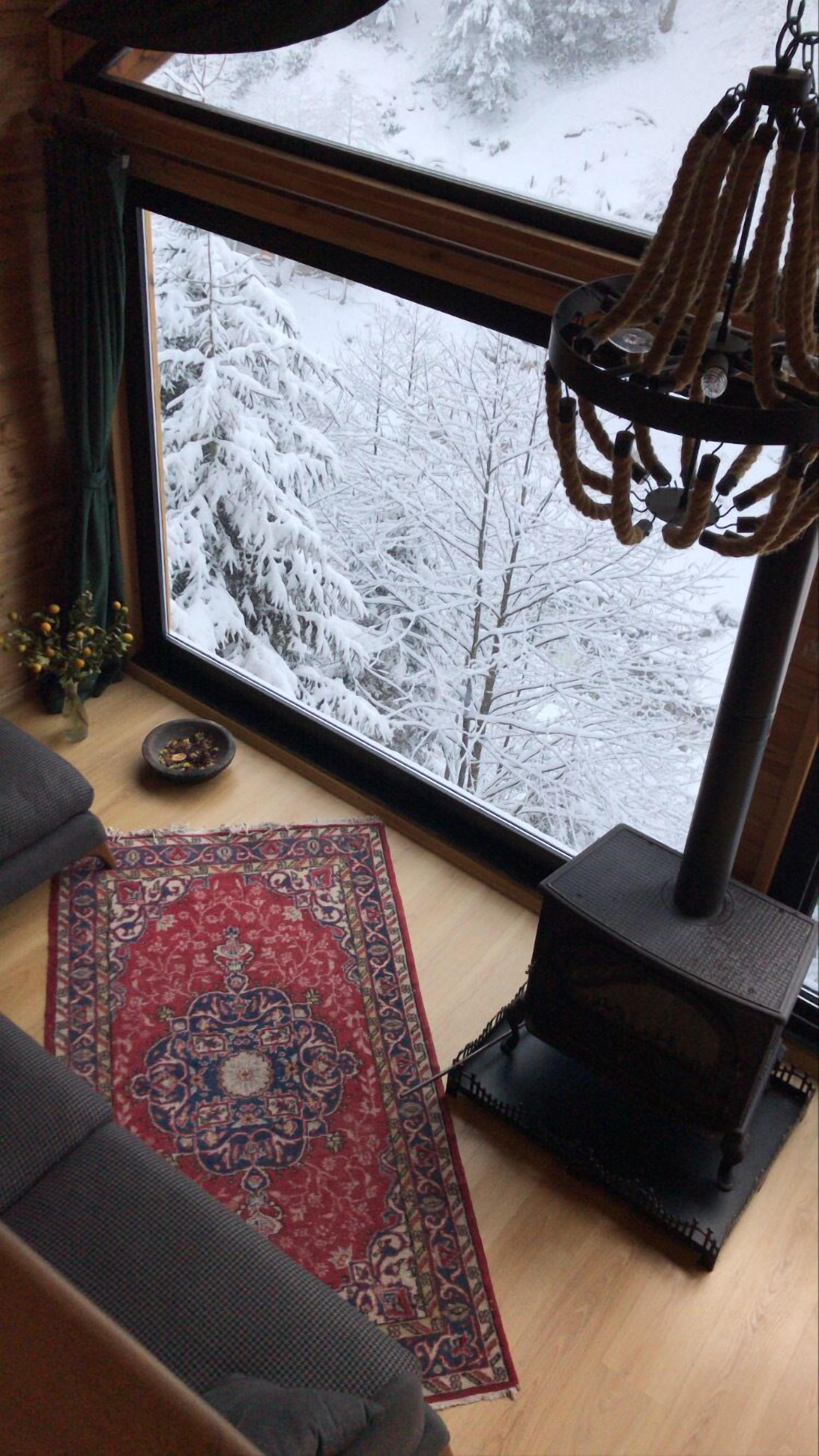 Una stanza accogliente con una grande finestra che si affaccia su un paesaggio innevato, un tappeto decorato e un camino a legna.