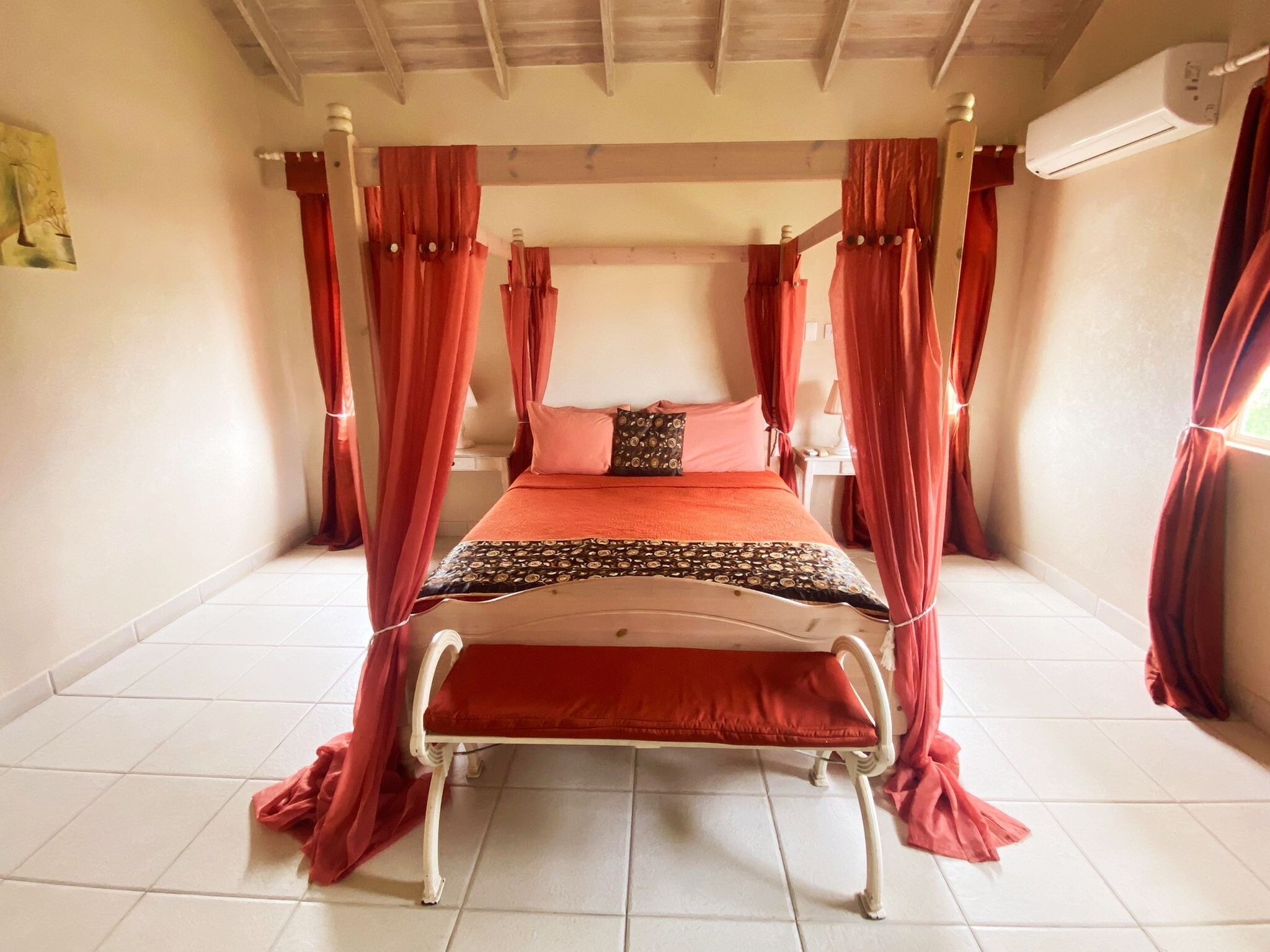 Un lit avec des rideaux rouges, une couvre-lit à motifs et un appareil de climatisation blanc fixé au mur.
