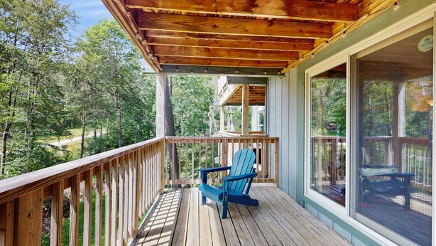 Eine Holzterrasse mit blauem Adirondack-Stuhl, einer Glastür und Blick auf ein bewaldetes Gebiet.