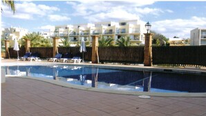 A swimming pool with lounge chairs and a tiled deck.