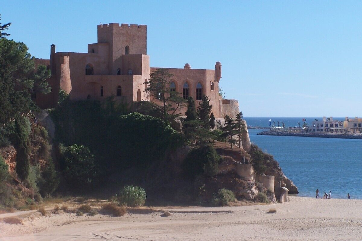 Un castello costiero con una torre imponente, arroccato su una scogliera a picco sul mare.