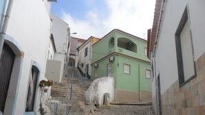 A narrow cobblestone street flanked by buildings with a staircase leading to a green building with a balcony.