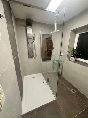 Ein modernes Badezimmer mit einer in Glas abgeschlossenen Dusche, einem integrierten Handtuchhalter und einem Blumentopf am Fensterbrett.
