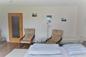 Ein Zimmer mit einem Bett, zwei Stühlen, einem kleinen Tisch und einer Tür.
