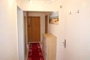 A hallway with a wooden door, a red carpet, a small wooden cabinet, and a painting on the wall.