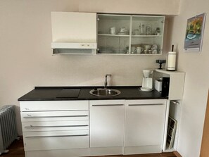 Eine kleine Küche mit Spüle, Kaffeemaschine und einem Schrank über der Arbeitsplatte.