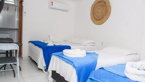 A clean, well-lit room with two beds, each with a blue towel and white linens. There is a small chair and a wall-mounted air conditioner. - Pousada Sereias de Maragogi (Maragogi)