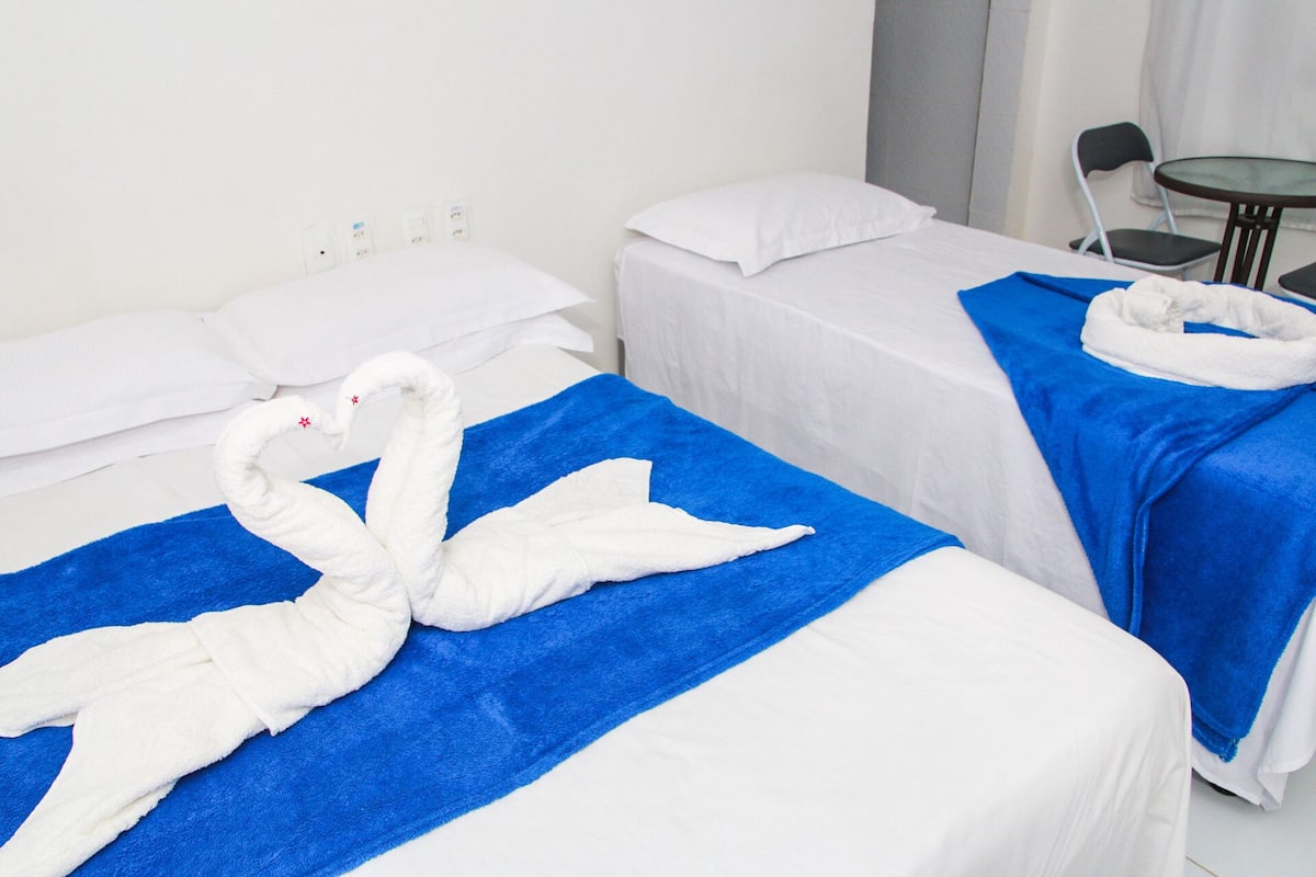 Dos camas de hotel con sábanas blancas y toallas azules; cada cama tiene una decoración de toalla con forma de cisne blanco.