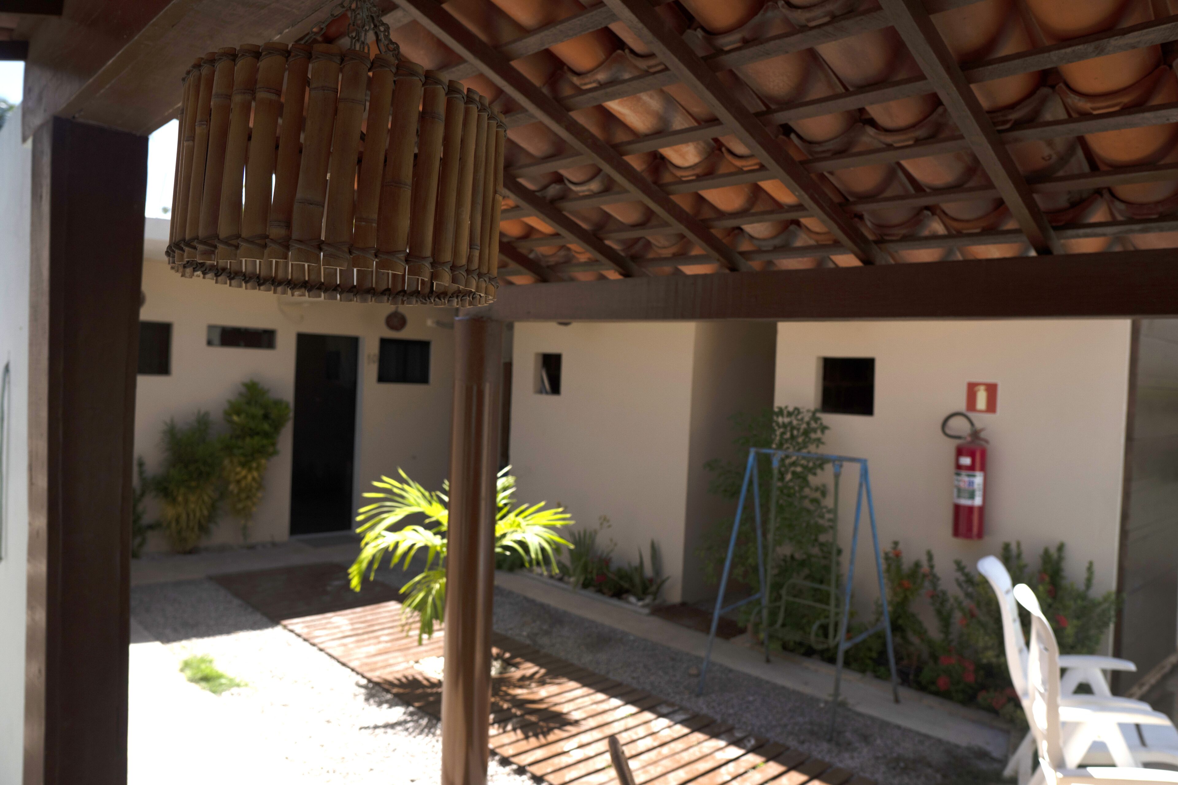 A covered outdoor area with a bamboo lamp, a fire extinguisher, and a small garden with plants and a swing set.