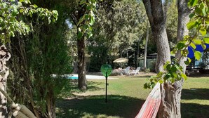 Eine Hängematze, die zwischen Bäumen in einer grünen Umgebung gespannt ist, mit einem Pool und Liegestühlen im Hintergrund.