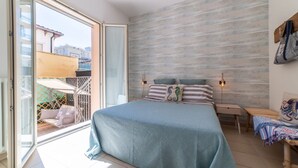 Une chambre avec un grand lit, une tête de lit en bois, une table de chevet, un banc et une vue sur le balcon extérieur.