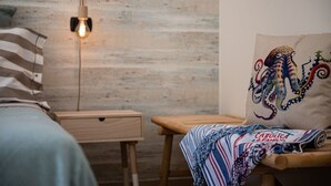 Une chambre à coucher avec une table de chevet en bois, une lampe, un lit avec une literie à rayures et un coussin coloré orné d’un motif de poulpe.