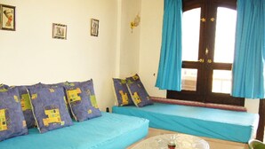 Ein Zimmer mit zwei blauen Betten, einem kleinen runden Tisch und einem Fenster mit blauen Vorhängen.