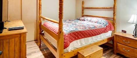 Ein hölzernes Himmelbett mit einer gesteppten Decke, ein Schreibtisch mit einem Computer, eine Lampe und eine kleine Holzkommode.