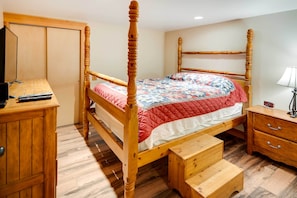 A wooden four-poster bed with a quilted bedspread, a wooden nightstand with a lamp, and a wooden cabinet with a television. - Ketchikan Apt - Walk to Refuge Cove Beach! (Ketchikan)