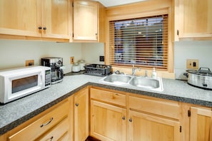 A kitchen with wooden cabinets, a granite countertop, a microwave, a coffee maker, a toaster, a sink, and a window with blinds. - Ketchikan Apt - Walk to Refuge Cove Beach! (Ketchikan)