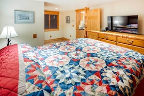 A bedroom with a large bed, a television, a wooden dresser, and a window with blinds. - Ketchikan Apt - Walk to Refuge Cove Beach! (Ketchikan)